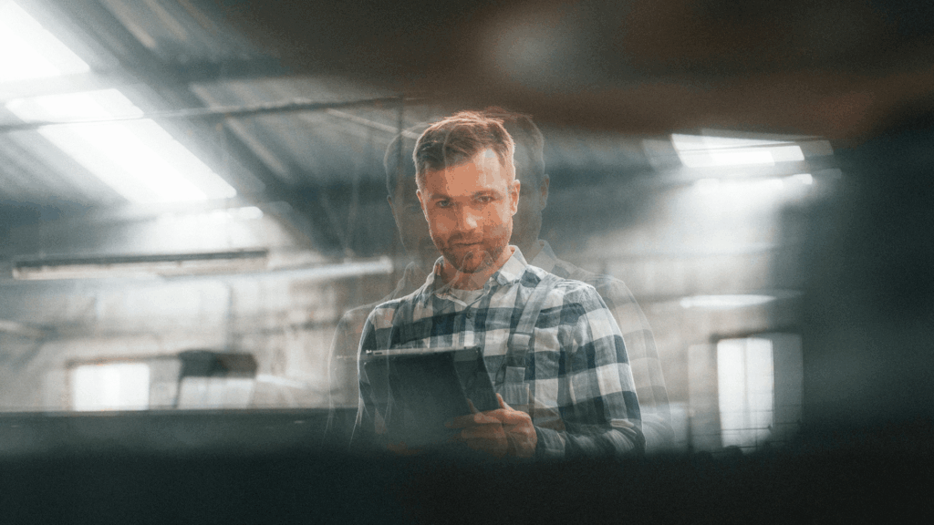 Man in checkered shirt using a tablet inside an industrial facility.
