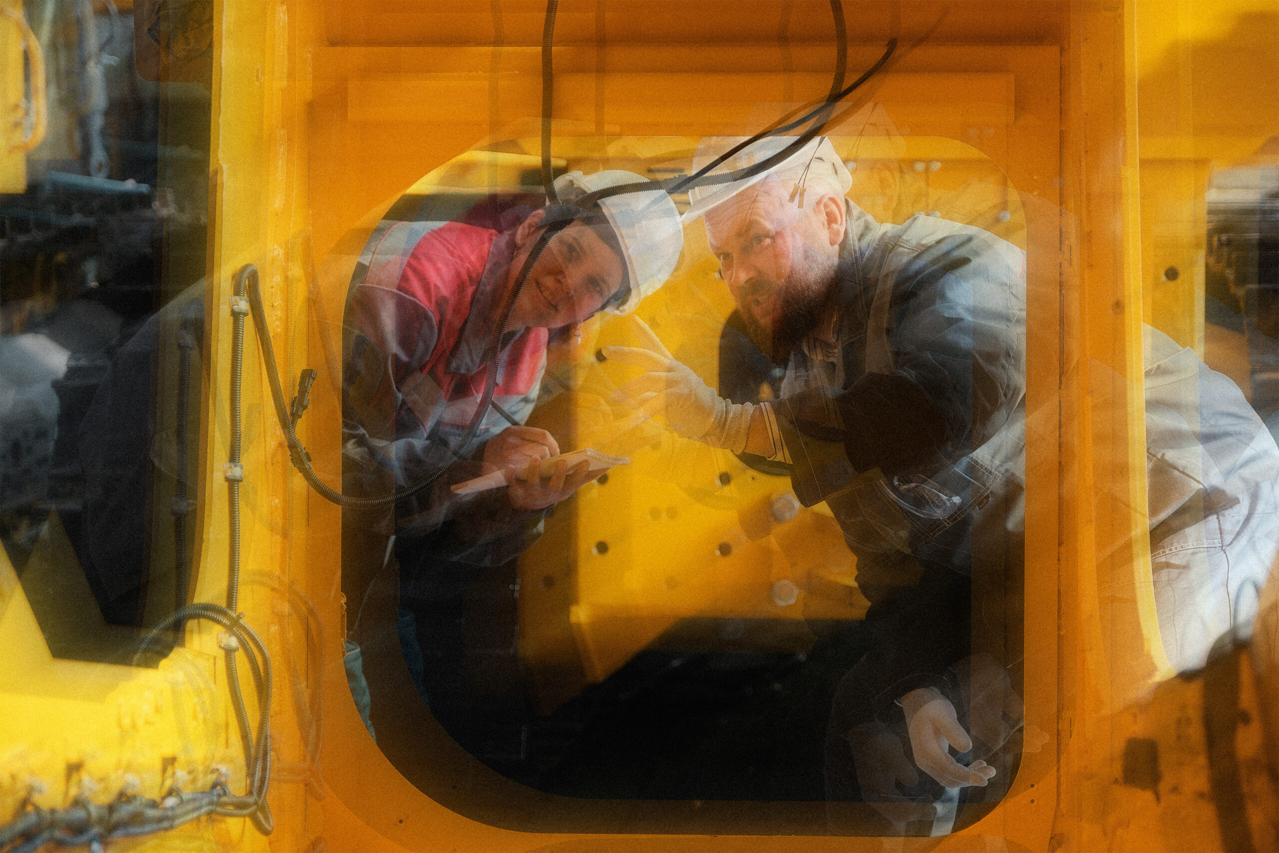 Two construction workers in white hard hats next to machinery