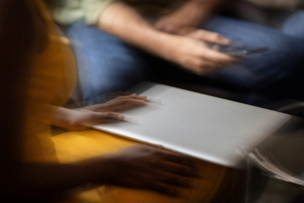 Blurry close-up of people using a laptop and smartphone, suggesting casual teamwork or tech collaboration.